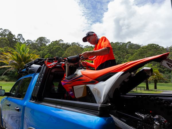 A dirt bike in the open tub of a RAM 1500 beside the canopy headboard