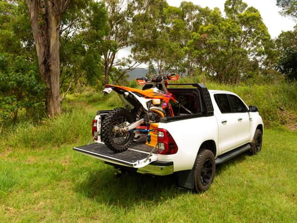 A white HiLux with a dirt bike in the open tub, canopy retracted