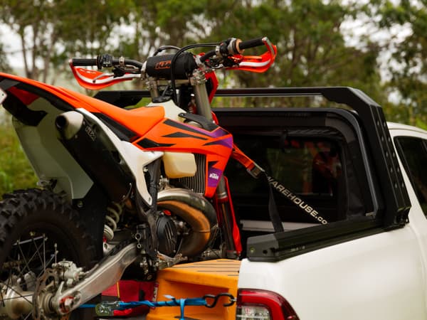 A dirt bike strapped into the open tub of a HiLux, canopy retracted