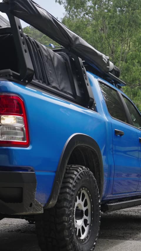 A tradie loads gear into the open tub of a blue RAM 1500 with the RCS canopy retracted